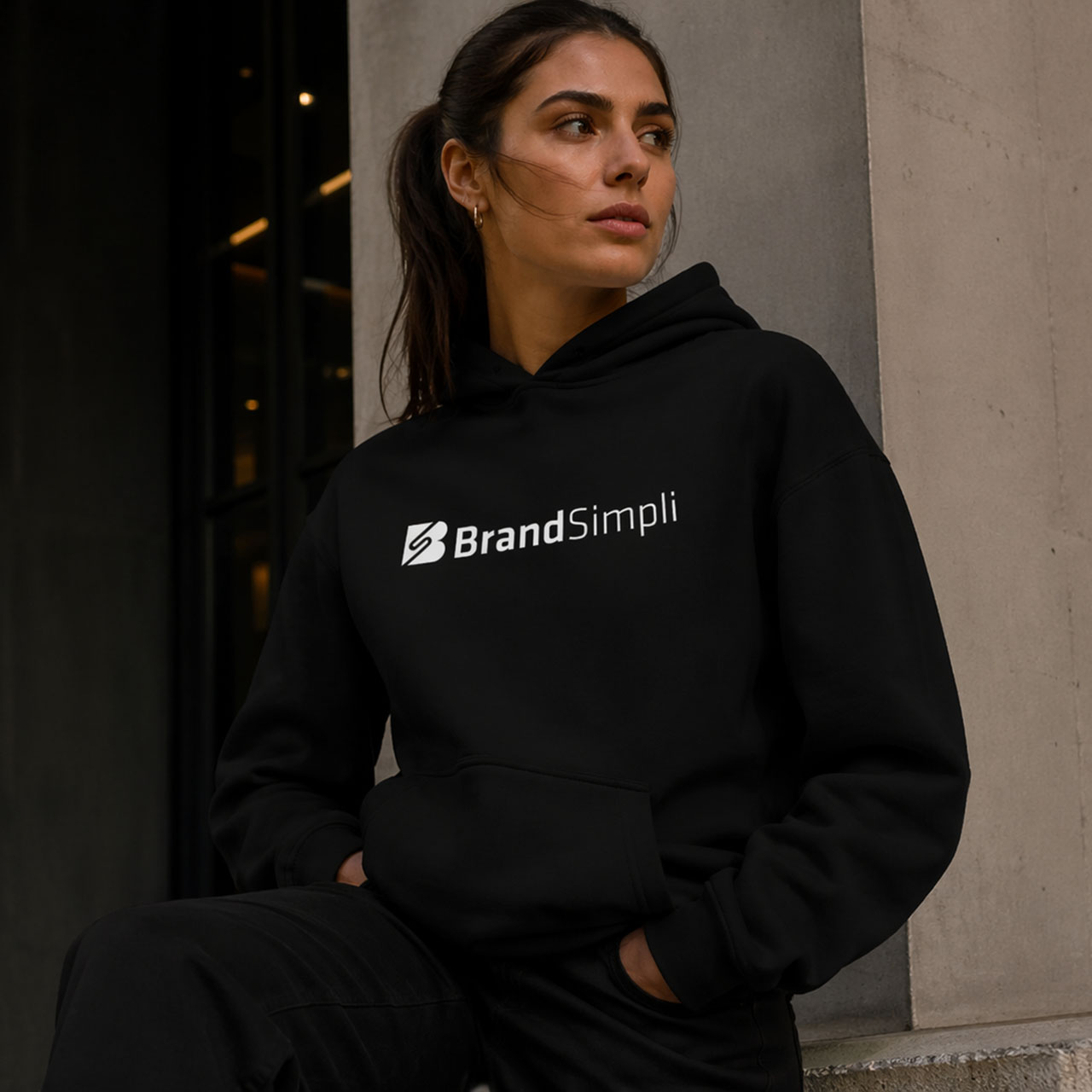 Frau trägt schwarze Hoodie mit BrandSimpli Logo, urbanes Umfeld.