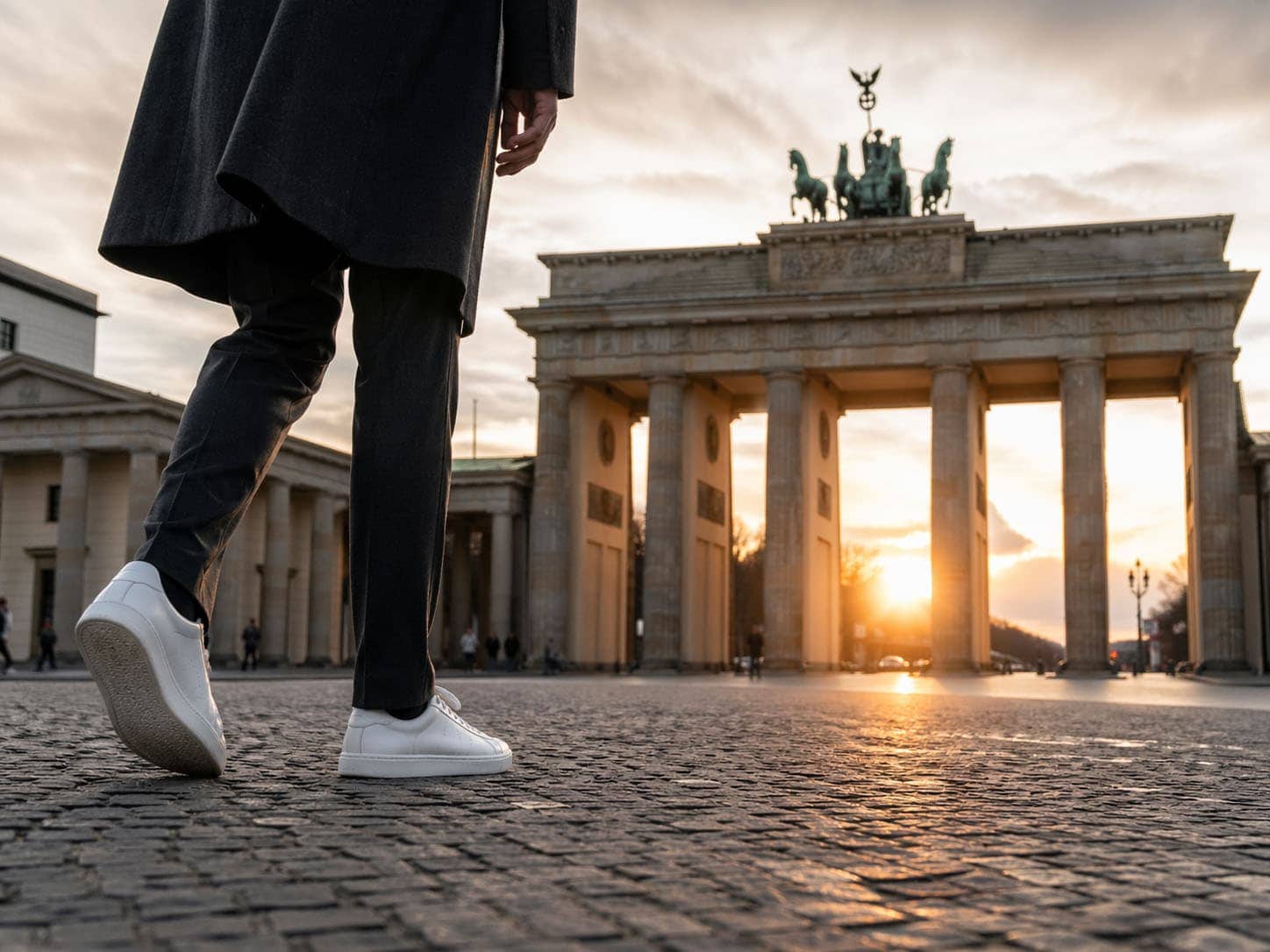 Person läuft am Brandenburger Tor in Berlin bei Sonnenuntergang vorbei.