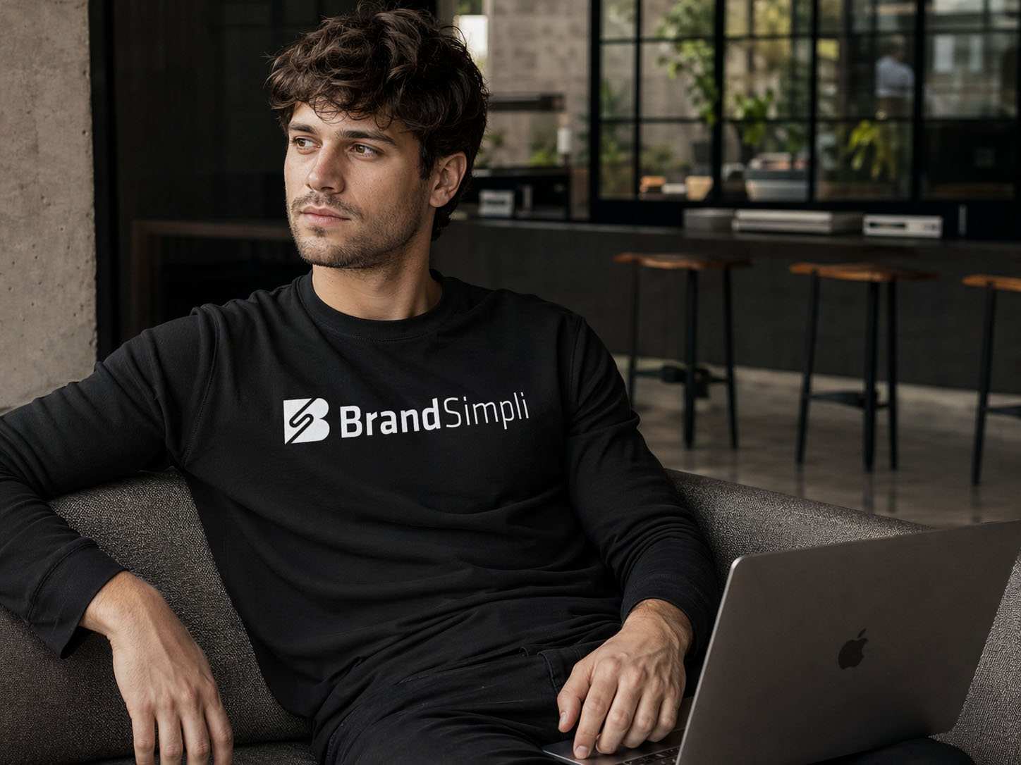 Mann trägt schwarzes T-Shirt mit BrandSimpli Logo, arbeitet am Laptop.