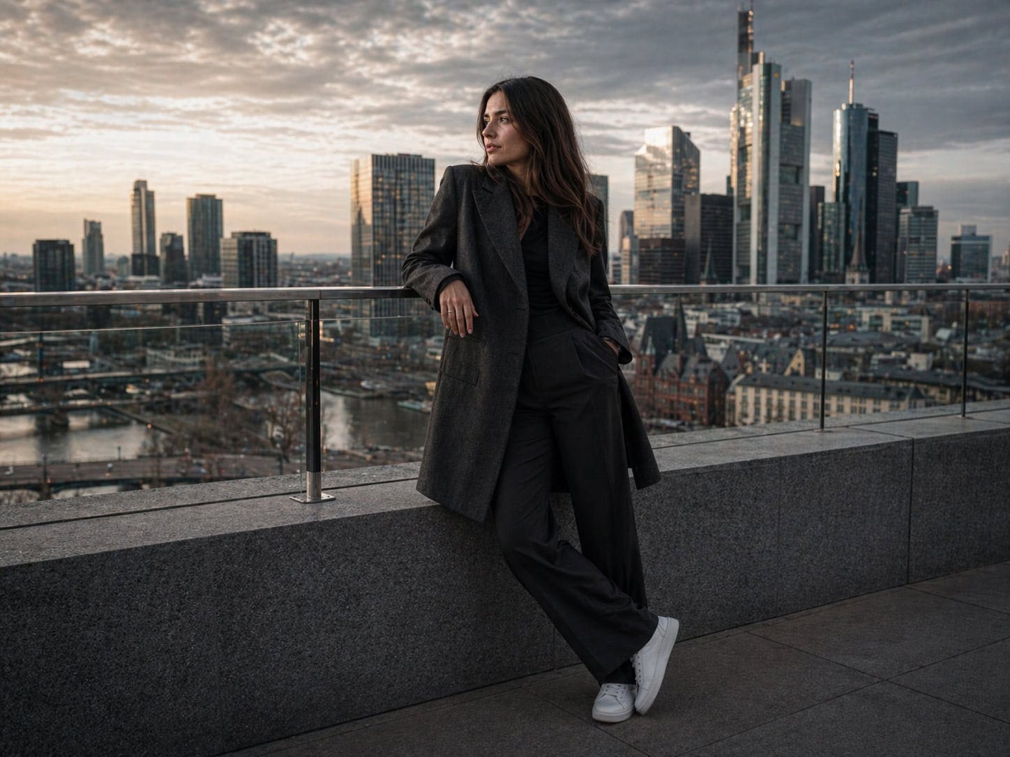 Frau in Business-Outfit auf Dach mit Skyline im Hintergrund.